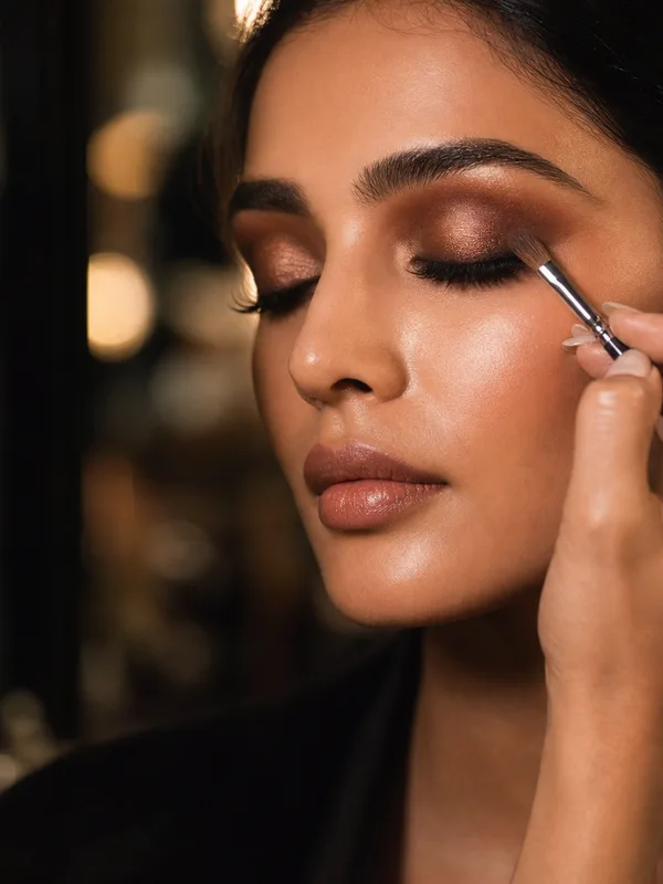A makeup artist applying eye makeup to a model backstage.