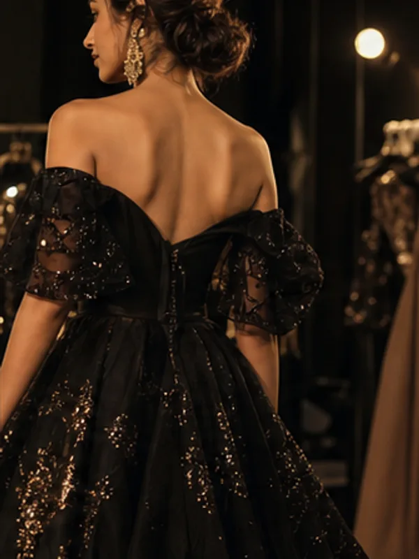 A model showing the back of a black sequined evening gown backstage.