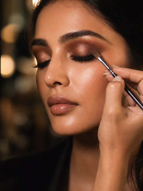 A makeup brush applying bronze eyeshadow to a model's closed eyelid.