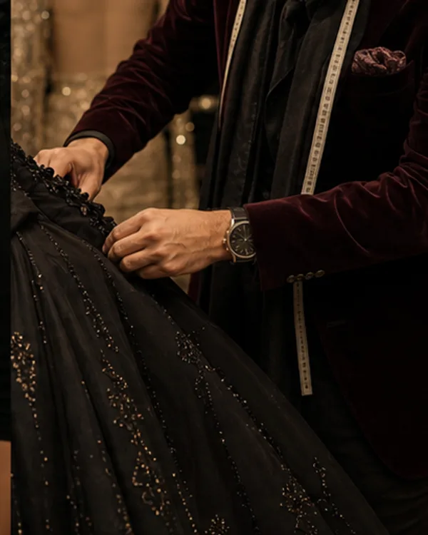 A designer's hands adjusting beaded detailing on a black gown.